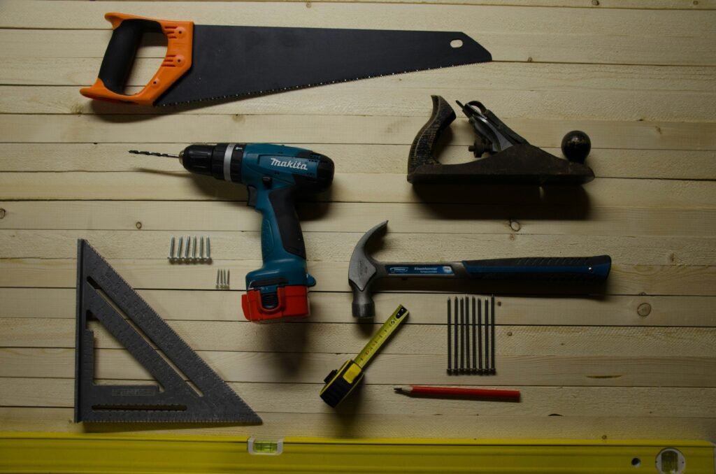 Collection of essential hardware tools including saw, drill, hammer, measuring tape, square, nails, and level on a wooden surface – Essential Hardware Too